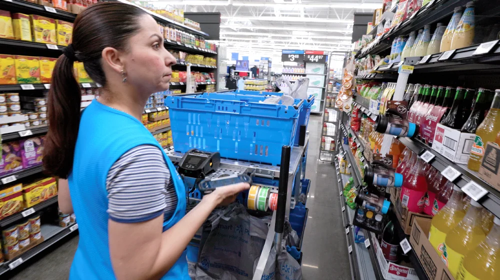 A Walmart associate picks an online order using a handheld device and blue collection bins.