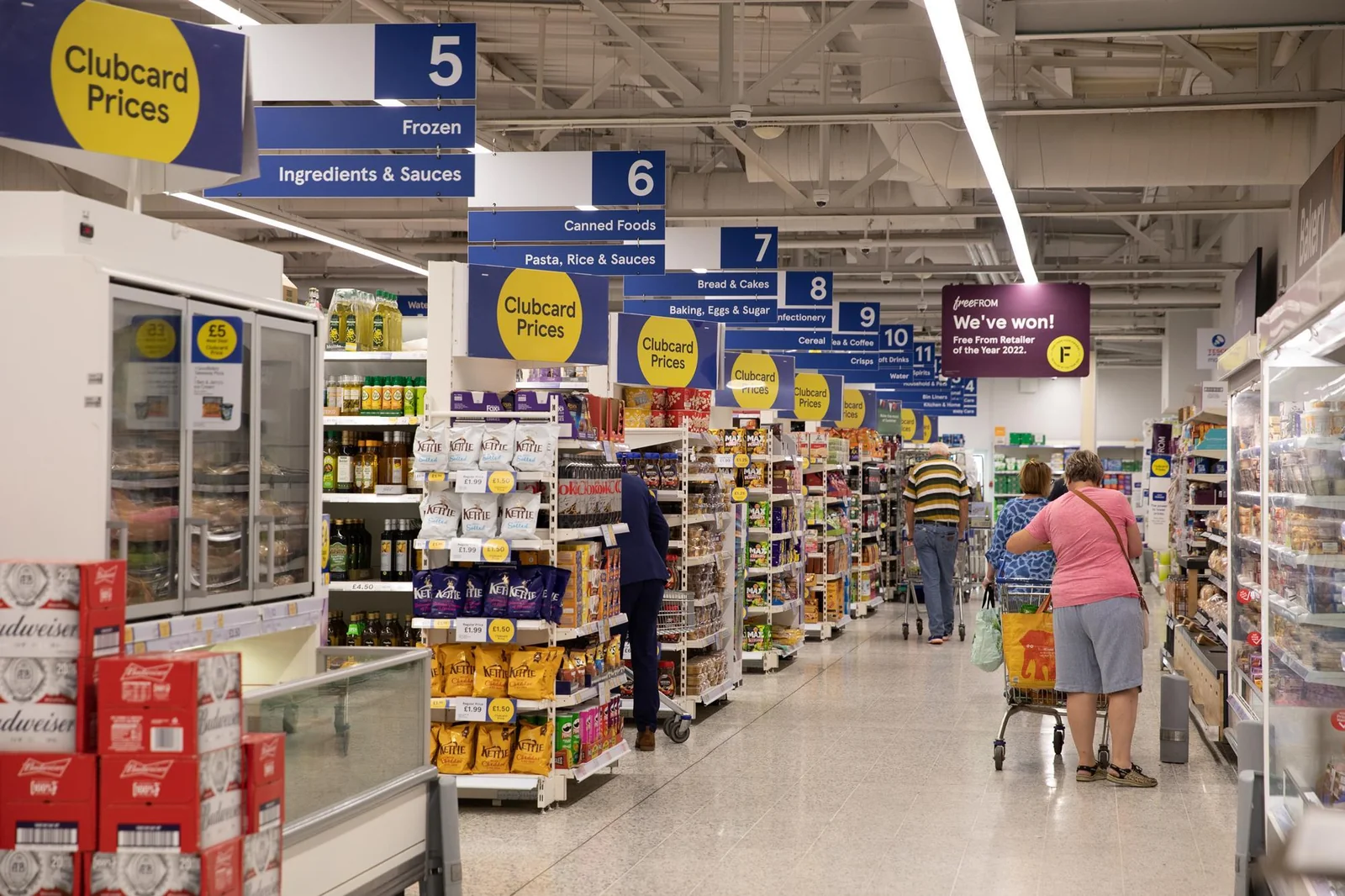 Shoppers in a Tesco aisle with recognisable blue and yellow promotional signage.